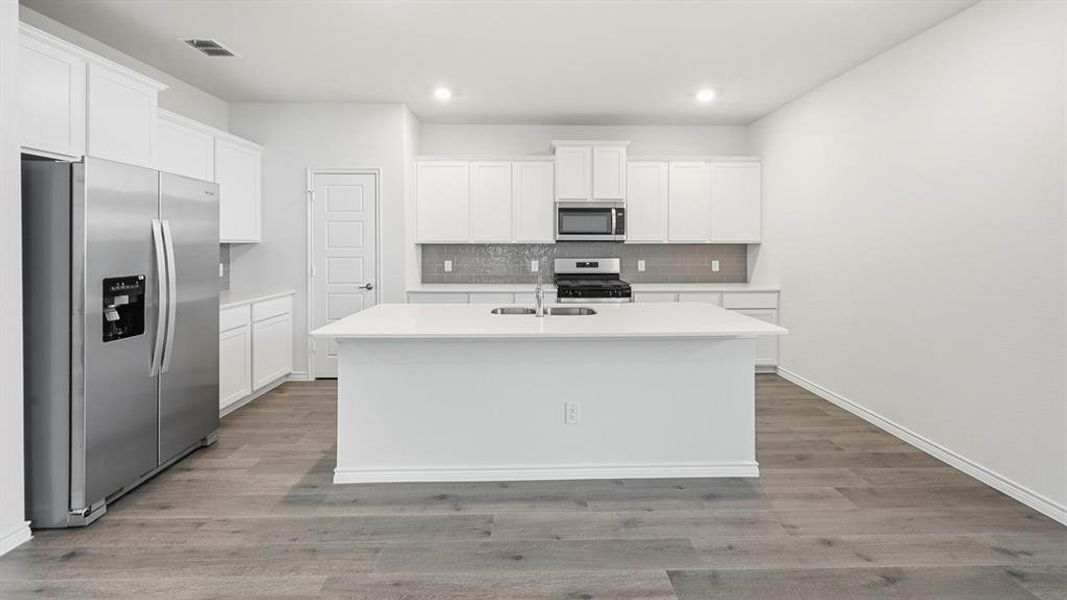 Kitchen featuring a central island with an undermount sink, white cabinetry, stainless steel appliances, a tile backsplash, and wood-finish flooring