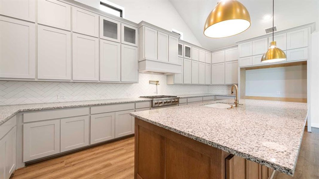 Kitchen with a center island with sink, stainless steel gas stovetop, sink, decorative backsplash, and light wood-type flooring