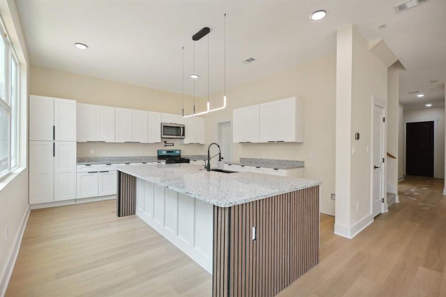 Kitchen featuring an island with sink, white cabinets, light stone counters, and sink