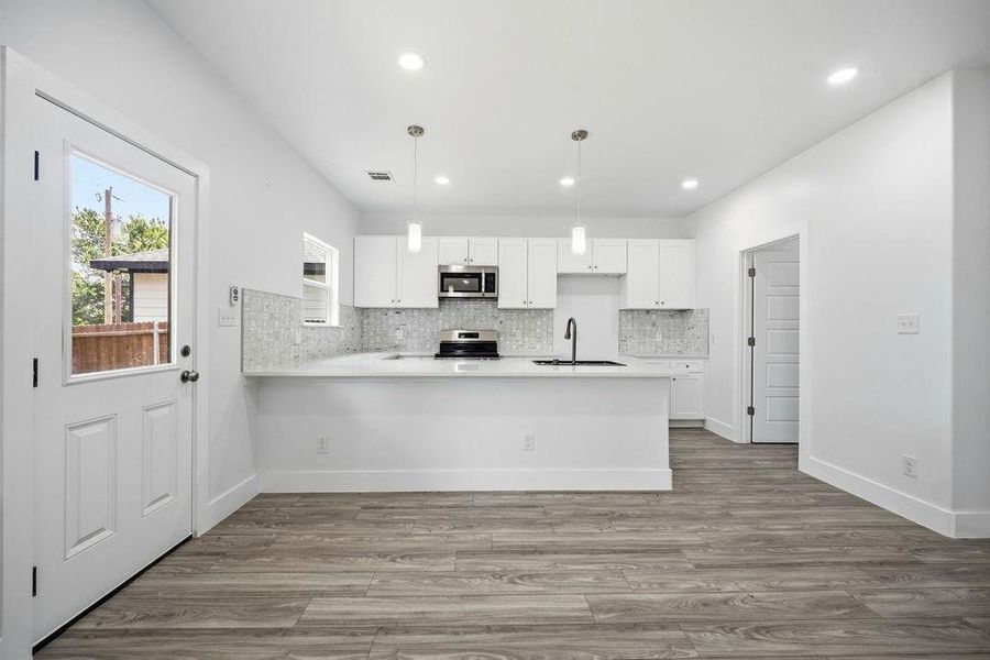 Open-concept kitchen featuring white cabinetry, a large kitchen island with counter seating, stainless steel appliances, and a mosaic tile backsplash Open-concept kitchen featuring white cabinetry, a large kitchen island with counter seating, stainless steel appliances, and a mosaic tile backsplash