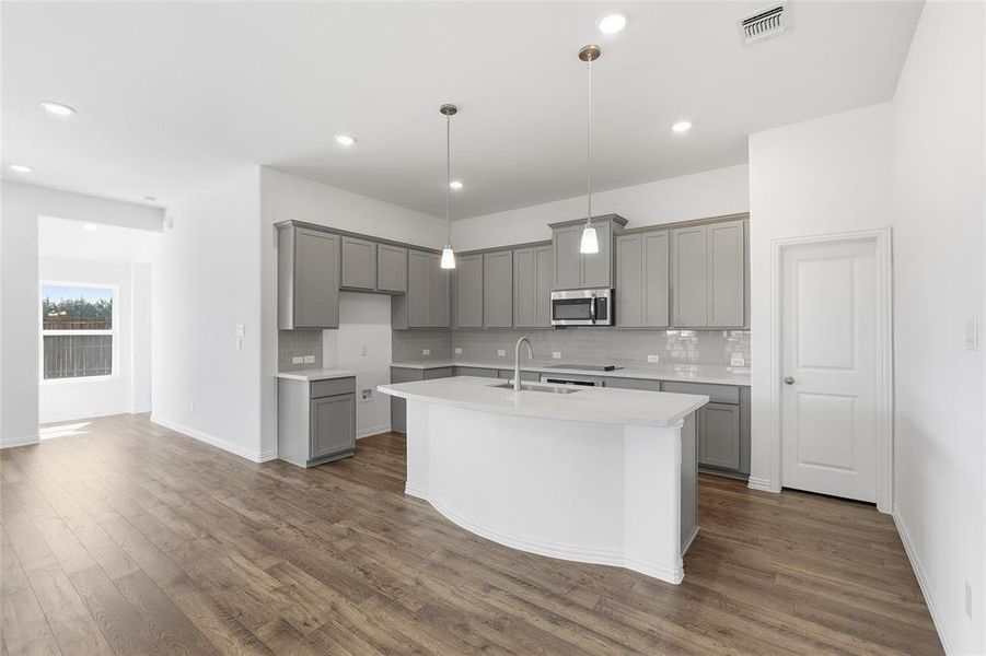 Modern kitchen featuring light gray cabinetry, white countertops, a central island with sink, stainless steel microwave, and wood-finish flooring