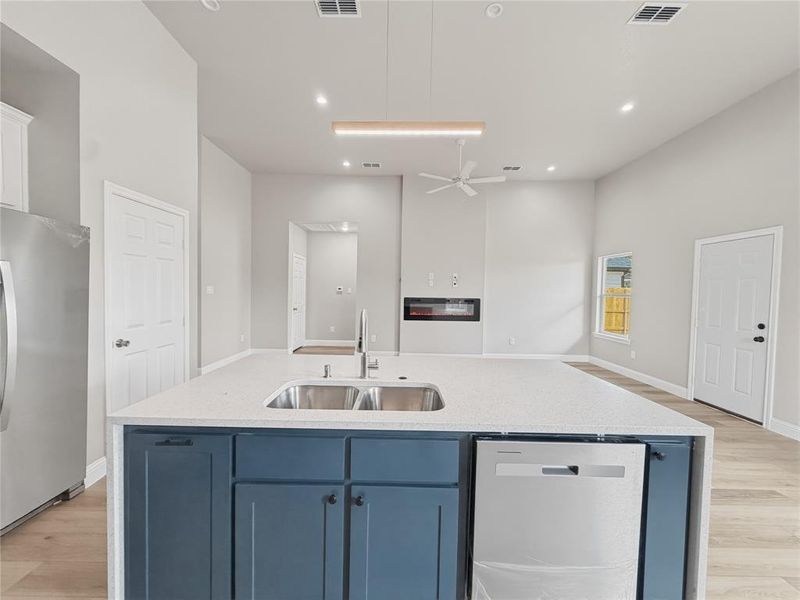 Kitchen featuring blue cabinets, light stone countertops, an island with sink, stainless steel appliances, and light wood-style flooring