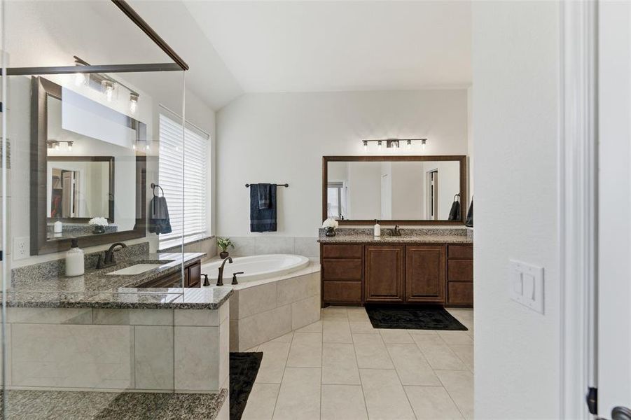 Full bath with two vanities, a garden tub, light tile patterned floors, and vaulted ceiling