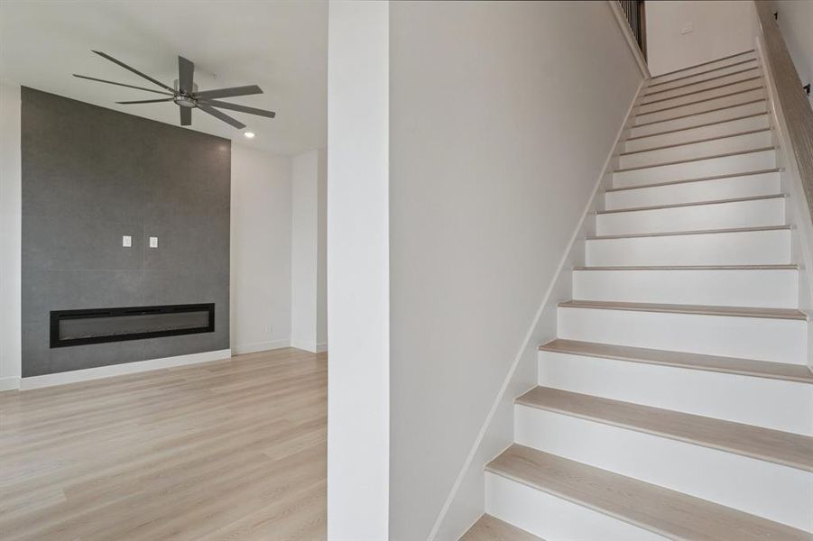 Stairs featuring wood finished floors, a large fireplace, ceiling fan, and recessed lighting