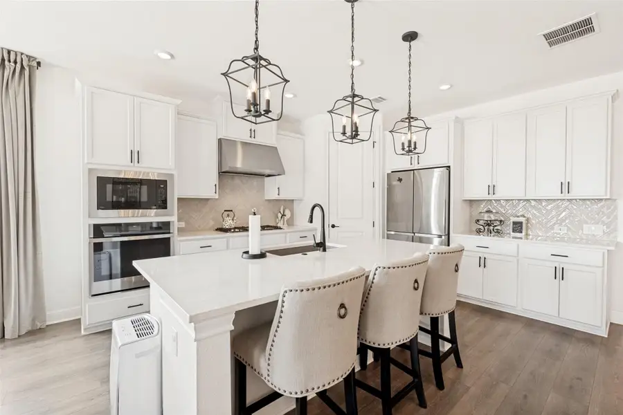 White cabinetry, stone counters, and wood-look flooring define this modern culinary space.