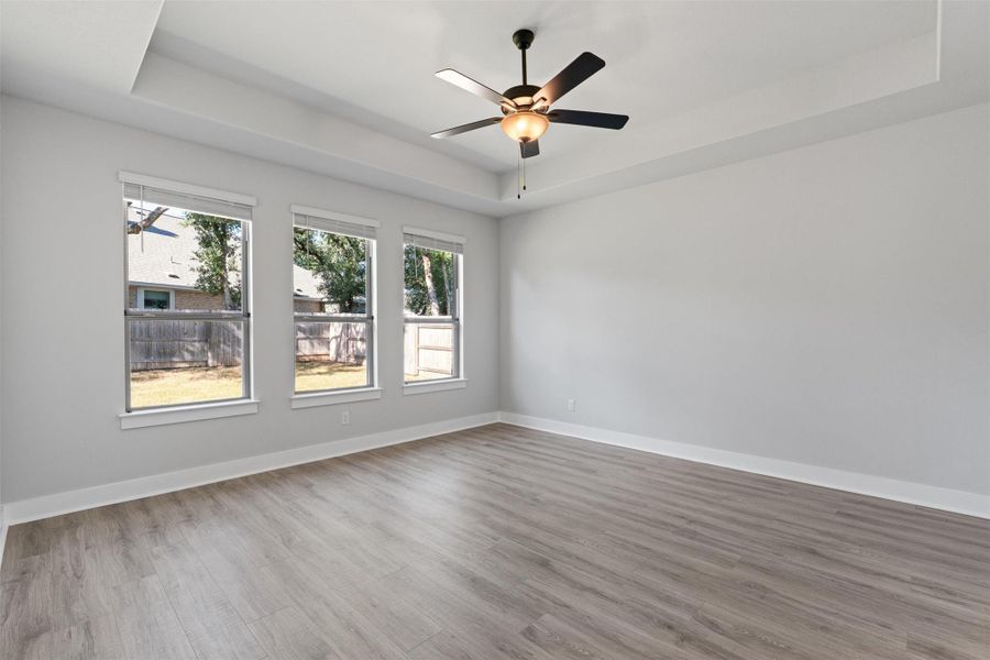 Empty room with a raised ceiling, wood finished floors, and a ceiling fan