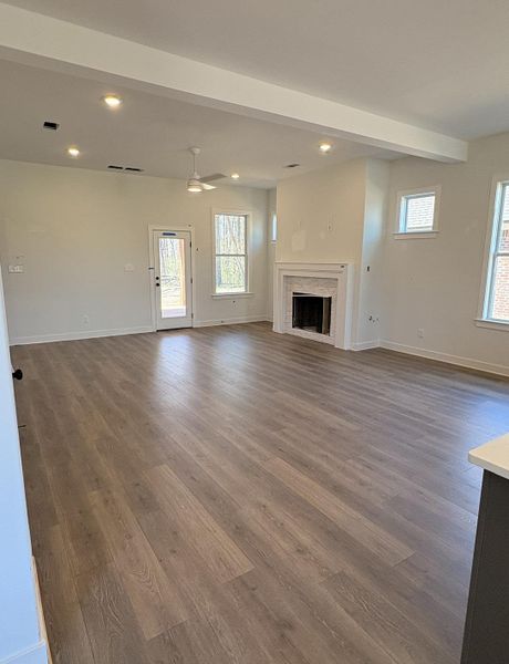 Unfurnished living room featuring dark wood-style flooring, recessed lighting, a fireplace, and beam ceiling