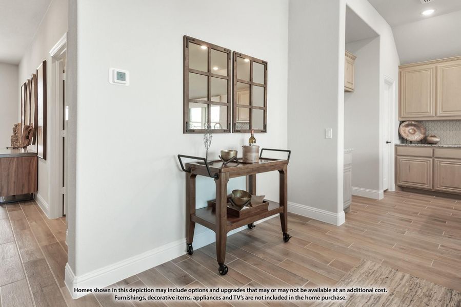 Hallway with wooden bar cart, two framed mirrors, and wood-look tile floors, with kitchen visible in background.