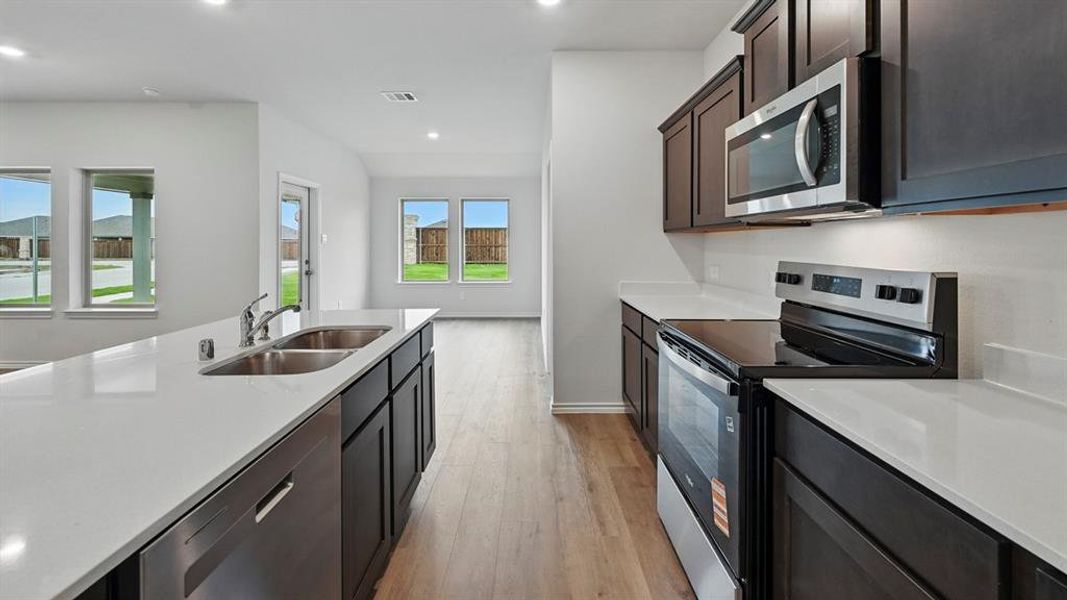 Kitchen featuring stainless steel appliances, dark wood finish cabinets, light wood-type flooring, recessed lighting, and light stone countertops