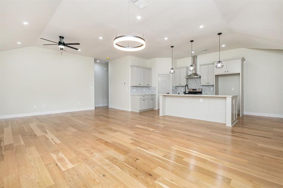 Unfurnished living room with visible vents, baseboards, light wood finished floors, lofted ceiling, and ceiling fan