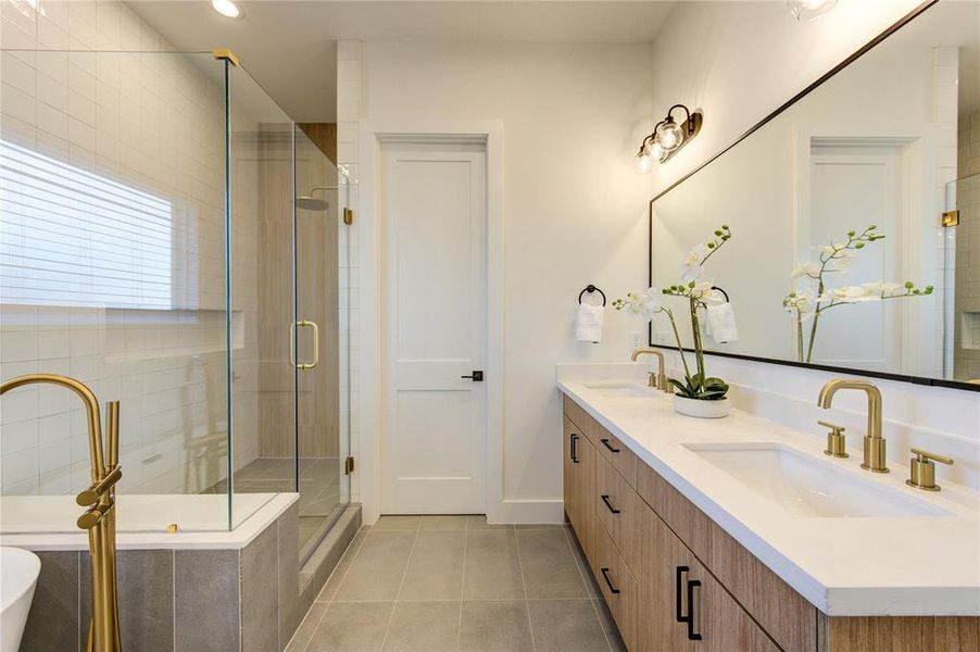 This primary bathroom feels like a spa with designer tile work, elegant champagne bronze fixtures, large soaking tub and walk-in shower, double vanity, and separated toilet room.