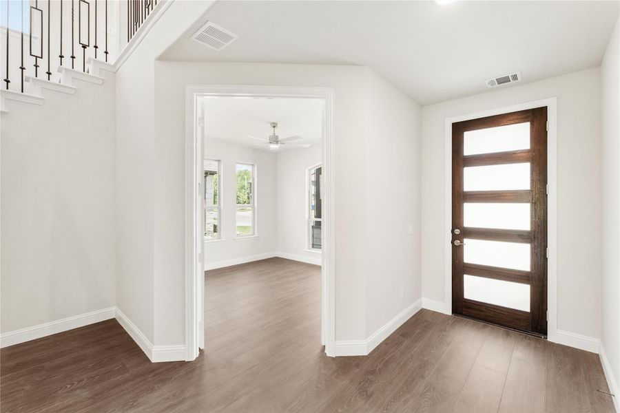 Entryway with dark wood front door, hardwood floors, and staircase leading to open living area
