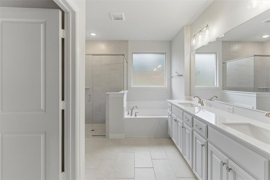 Bathroom featuring a dual vanity with white cabinetry, a built-in tub, a separate glass-enclosed shower, and tiled flooring