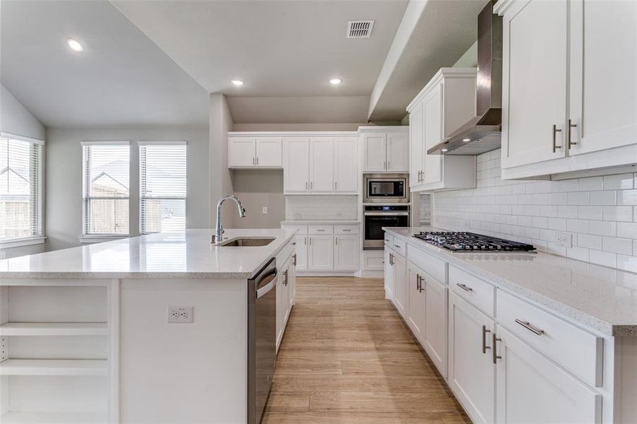 Kitchen with tasteful backsplash, stainless steel appliances, sink, light wood-type flooring, and wall chimney exhaust hood