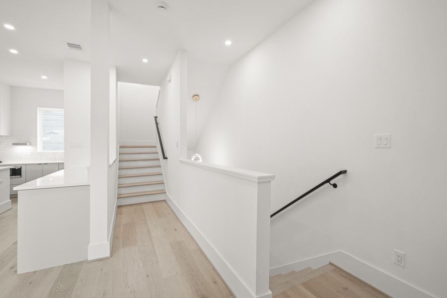 The second floor landing features a staircase with hardwood treads accented by a handrail that leads to the upper level. The stairway is illuminated by a decorative chandelier and a fixed window which keeps the area bright and welcoming.