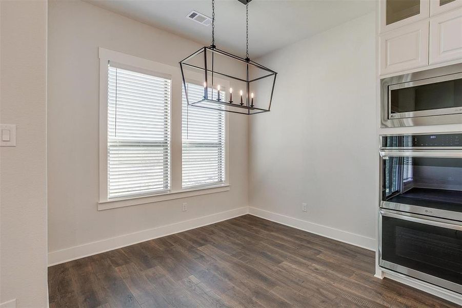 Unfurnished dining area featuring dark hardwood / wood-style floors, a healthy amount of sunlight, and a notable chandelier