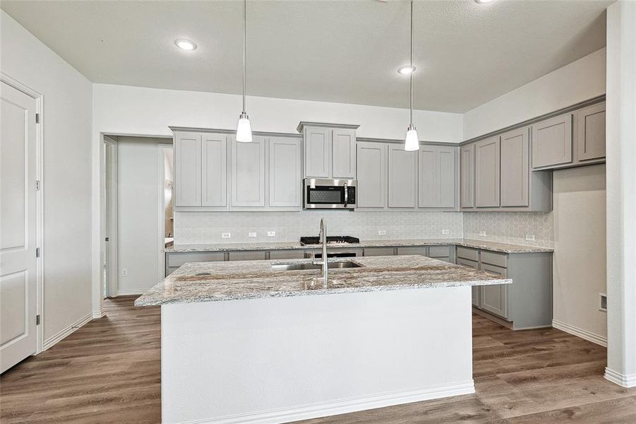 Kitchen with a center island with sink, hanging light fixtures, appliances with stainless steel finishes, light stone countertops, and dark wood-type flooring