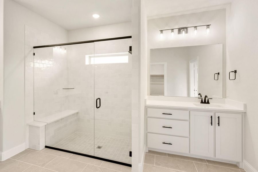 Bathroom with glass walk-in shower, built-in bench, white vanity, and black hardware accents