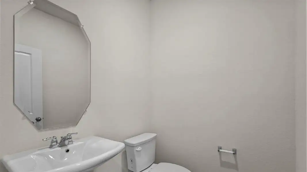 Well-appointed powder room featuring an octagonal mirror above a pedestal sink with chrome fixtures, complemented by a toilet and a wall-mounted toilet paper holder