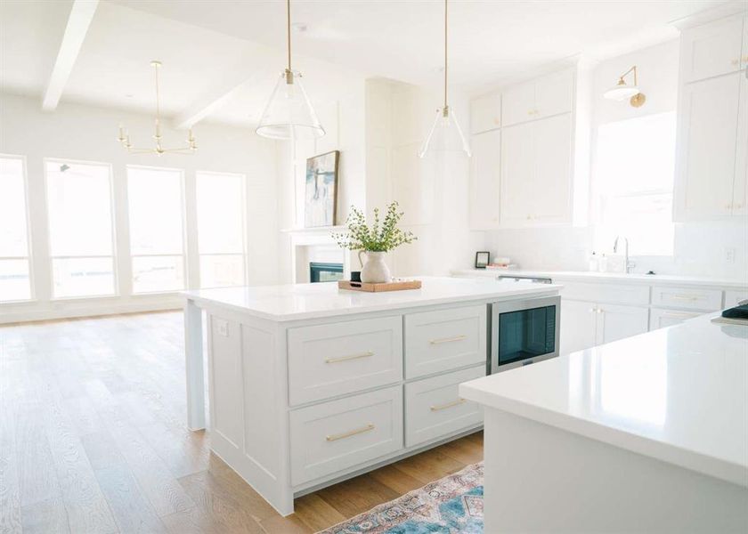 Kitchen with decorative light fixtures, light hardwood / wood-style floors, stainless steel microwave, beamed ceiling, and white cabinets