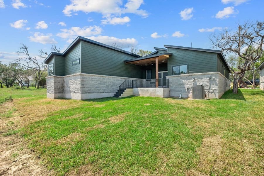 Rear view of property featuring a yard, stone siding, a patio area, and stairs Rear view of property featuring a yard, stone siding, a patio area, and stairs