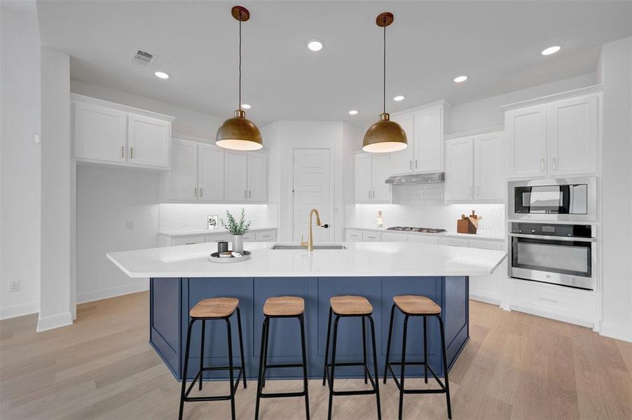 Kitchen with a kitchen breakfast bar, oven, dual tone cabinetry, light wood finished floors, and a large island with sink