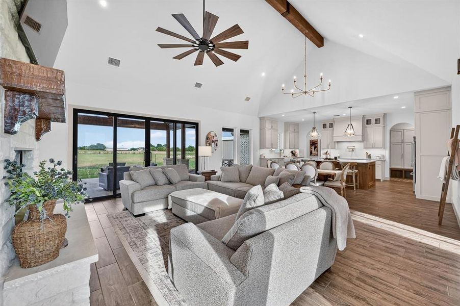 Spacious living area featuring high vaulted ceilings with exposed wood beams, a large sliding glass door system, and wood-finish flooring