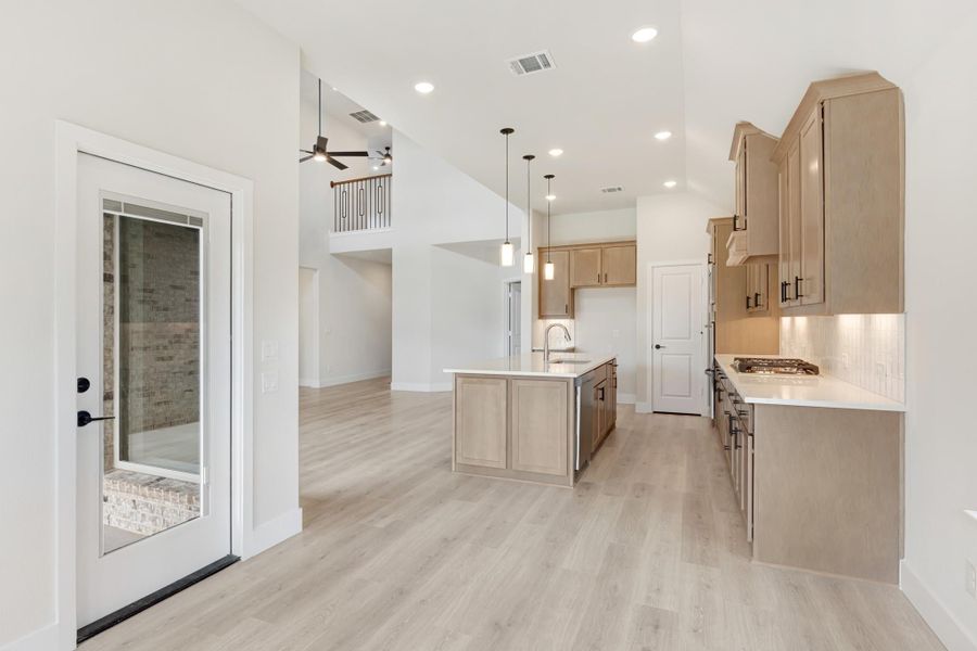 Open kitchen with tan wood cabinets, center island, and light hardwood floors open to two-story living area