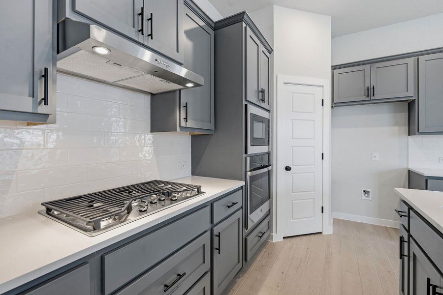 Modern kitchen features grey cabinetry and stainless steel appliances with light wood-style flooring.