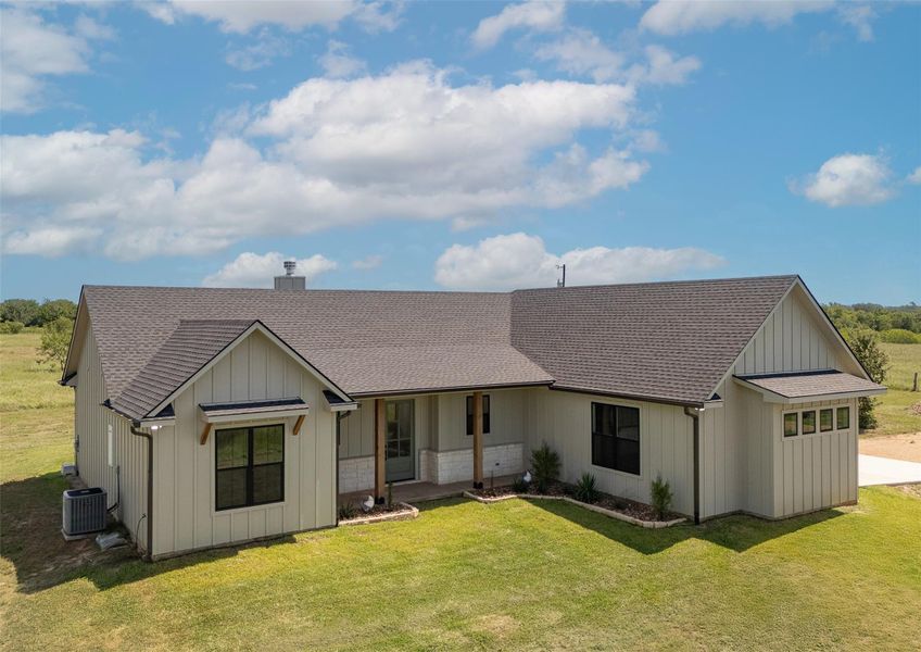 Rear view of property with a shingled roof, a lawn, and a porch