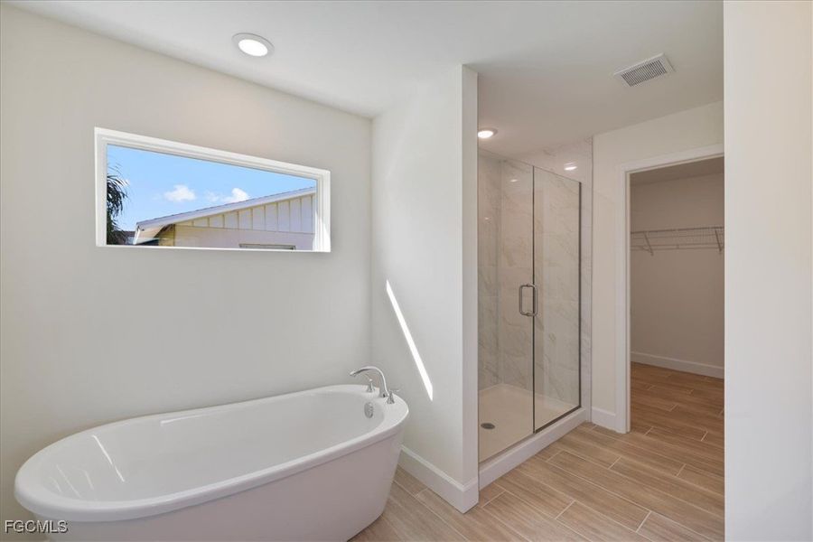 Bathroom featuring a spacious closet, a soaking tub, wood tiled floors, a marble finish shower, and recessed lighting