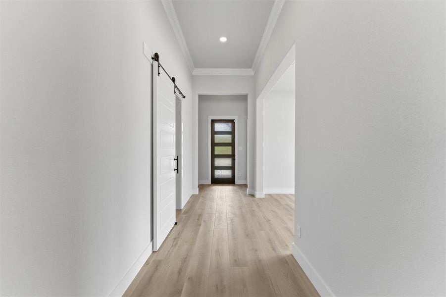 Hallway with a barn door, ornamental molding, light wood-style floors, and recessed lighting