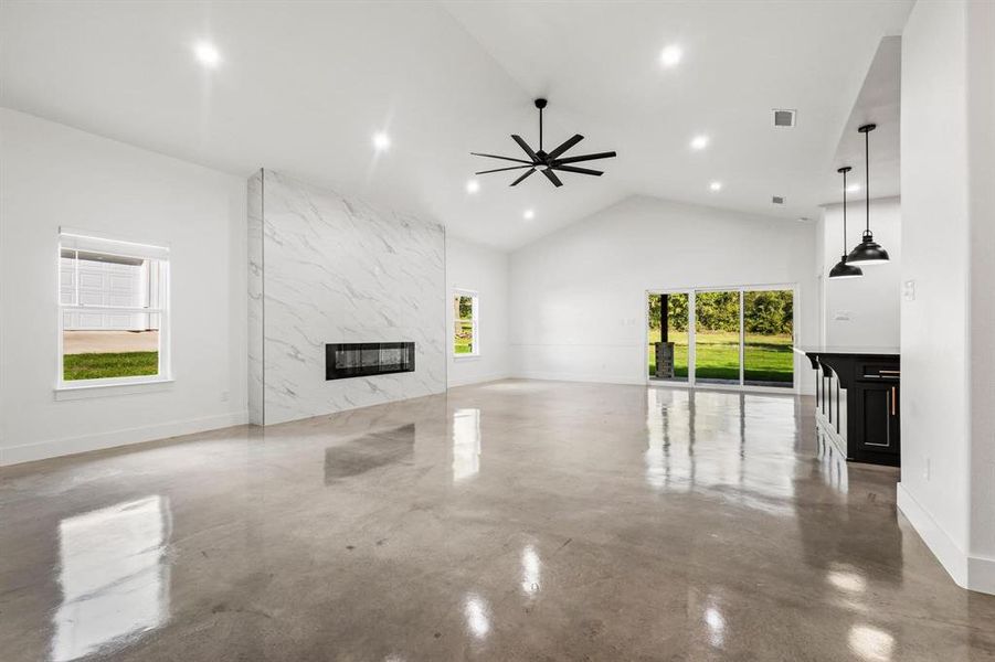 Unfurnished living room with a high end fireplace, concrete flooring, high vaulted ceiling, ceiling fan, and recessed lighting