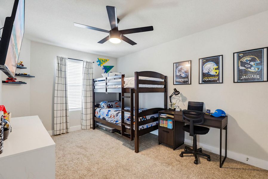 Carpeted room featuring a ceiling fan with integrated lighting, a window with blinds and grid-patterned curtains, and built-in shelving