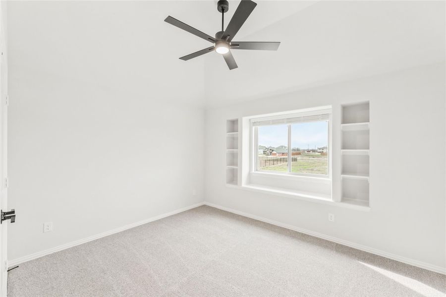 Empty bedroom with carpet, ceiling fan, large window, and built-in shelves on each side Empty bedroom with carpet, ceiling fan, large window, and built-in shelves on each side