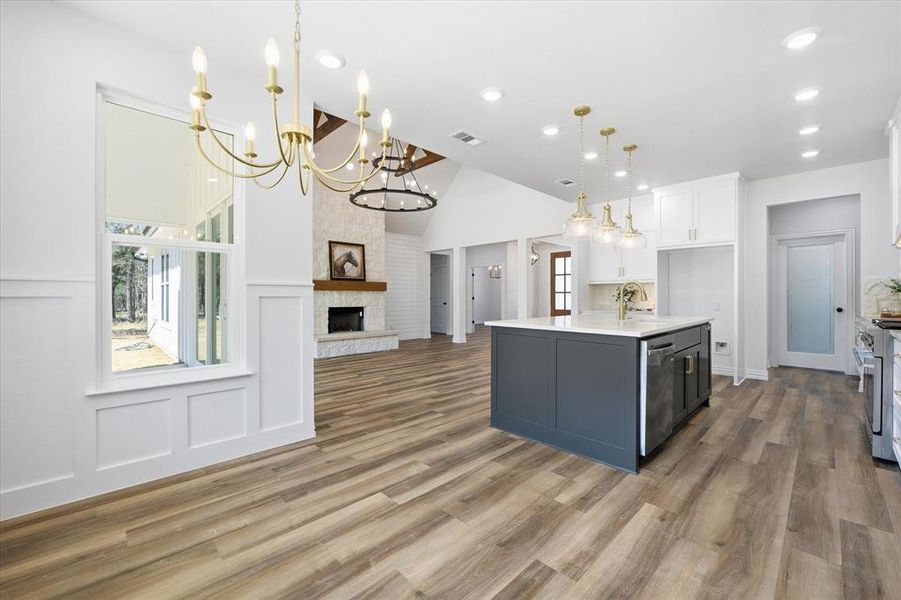 Two tone kitchen with dual tone cabinets, open floor plan, a stone fireplace, a kitchen island with sink, and dark wood-type flooring
