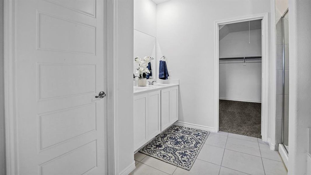 Full bath featuring vanity, a stall shower, light tile patterned floors, a walk in closet, and light colored carpet