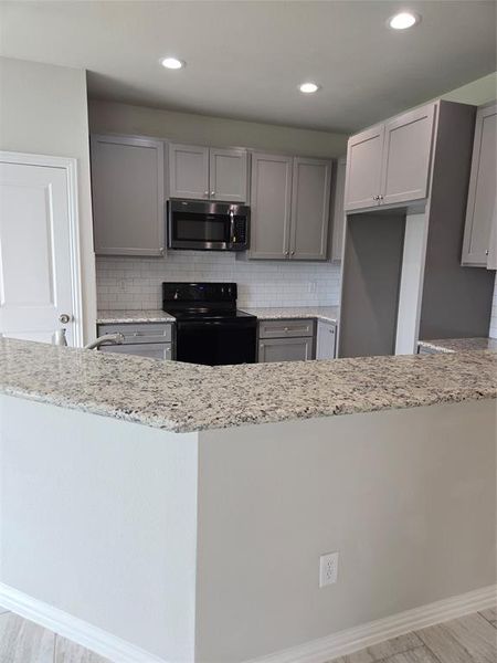 Kitchen with backsplash, gray cabinetry, light stone countertops, and electric range oven