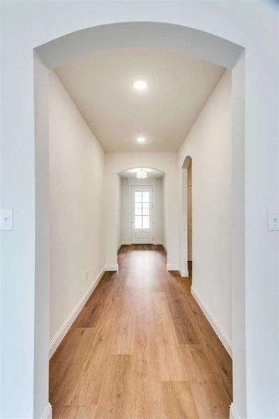 Corridor with arched walkways, light wood-style floors, and baseboards