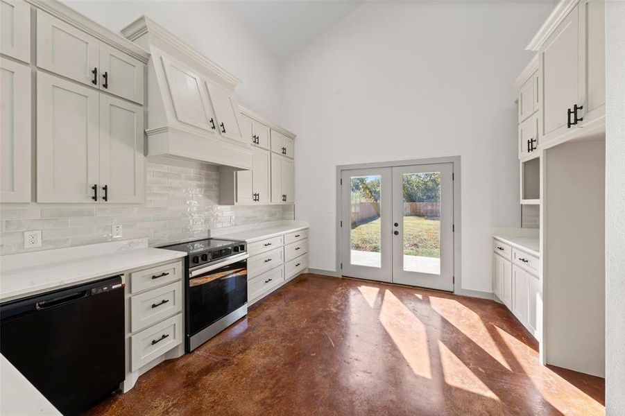 Kitchen featuring black dishwasher, concrete flooring, electric range oven, tasteful backsplash, and white cabinetry