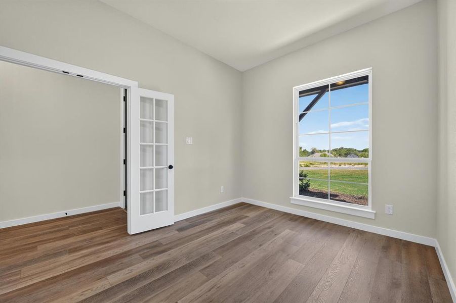 Bright interior room featuring wood-finish flooring, white baseboards, and a large window with white framing Bright interior room featuring wood-finish flooring, white baseboards, and a large window with white framing