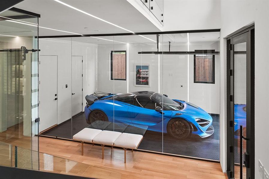 Glass-enclosed showroom garage featuring track lighting, white walls, and a dark textured floor