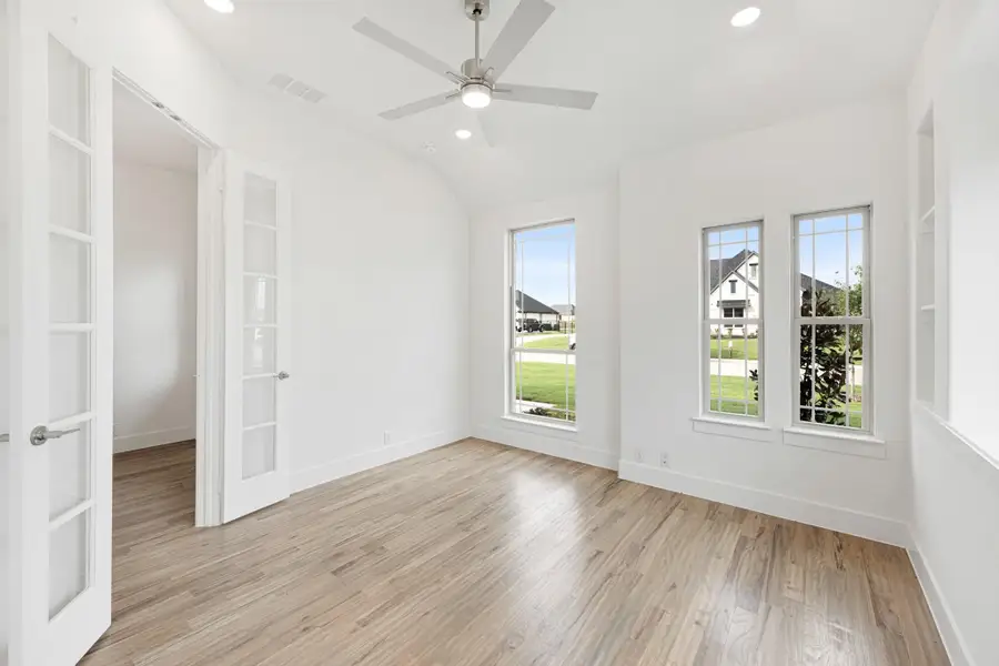 Empty room with hardwood floors, ceiling fan, vaulted ceiling, and French doors with large windows Empty room with hardwood floors, ceiling fan, vaulted ceiling, and French doors with large windows