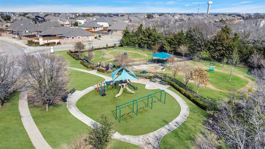 Expansive green space featuring a playground with slides and swings, shaded seating areas, winding concrete pathways, and surrounding residential properties