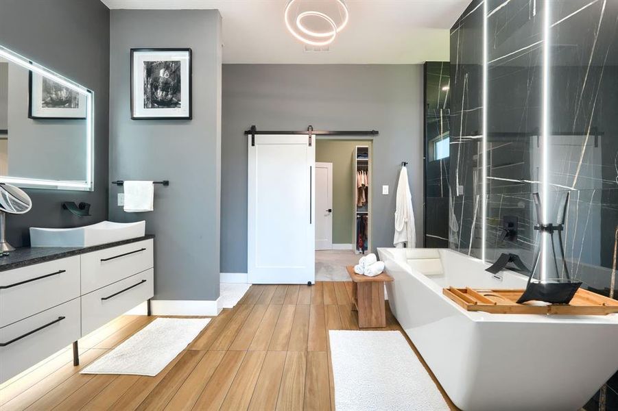 Full bathroom with vanity, a soaking tub, a walk in closet, a stall shower, and light wood-style flooring Full bathroom with vanity, a soaking tub, a walk in closet, a stall shower, and light wood-style flooring