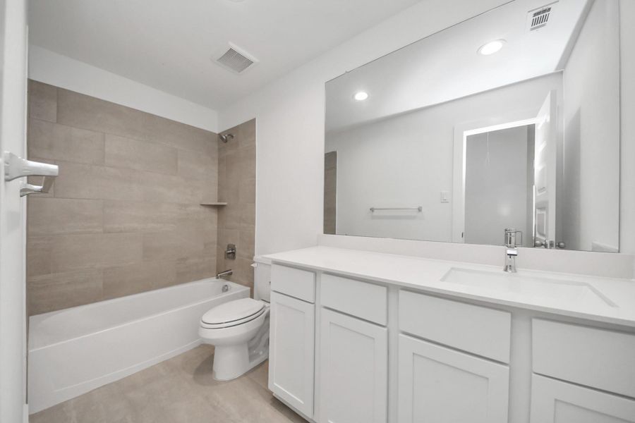 Secondary bath features tile flooring, bath/shower combo with tile surround, light stained wood cabinets, beautiful light countertop. Sample photo of completed home with similar floor plan. Actual colors and selections may vary. Secondary bath features tile flooring, bath/shower combo with tile surround, light stained wood cabinets, beautiful light countertop. Sample photo of completed home with similar floor plan. Actual colors and selections may vary.