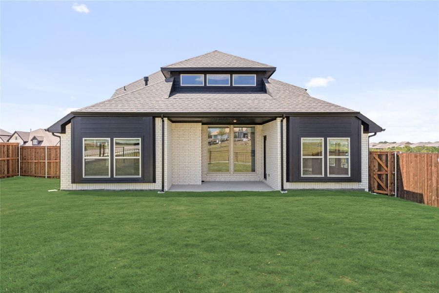 Rear exterior of single-story home with brick and dark siding, covered patio, large windows, and fenced backyard