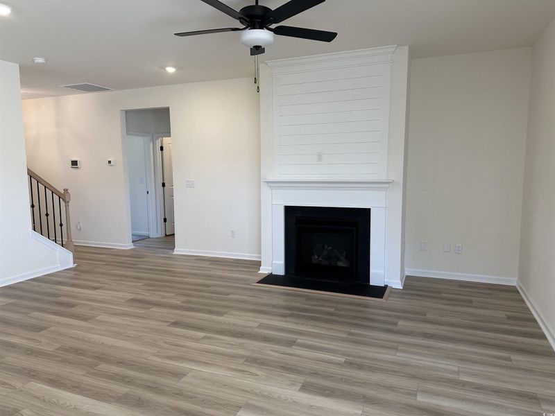 Unfurnished living room with a large fireplace, stairs, ceiling fan, light wood-style flooring, and recessed lighting