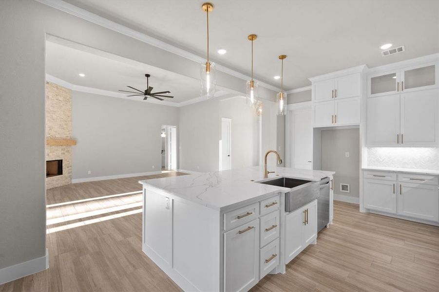 Kitchen with ceiling fan, sink, white cabinets, and an island with sink