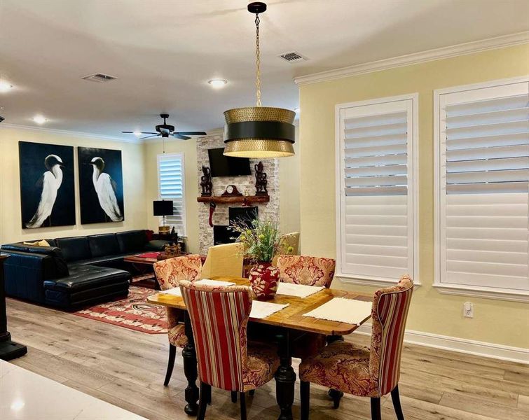 Dining space with crown molding, a stone fireplace, hardwood / wood-style floors, and ceiling fan